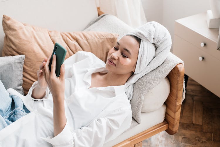 A Woman In A Head Towel Using A Mobile Phone On A Couch