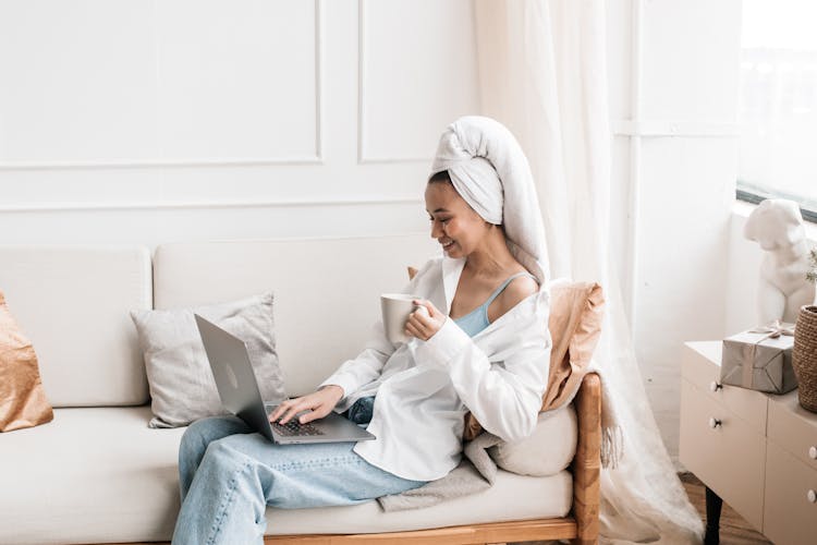 A Woman In A Head Towel Using Her Laptop While Sitting On A Couch