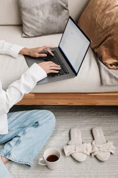 Comfortable home workspace with laptop, coffee, and slippers for a cozy work environment.