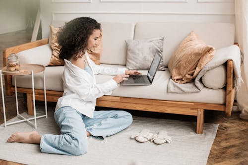 Woman Sitting on Floor Using Laptop on Couch