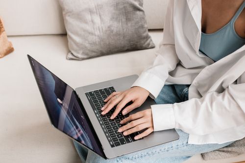 Free Casual scene of a woman typing on a laptop while sitting on a couch at home. Stock Photo