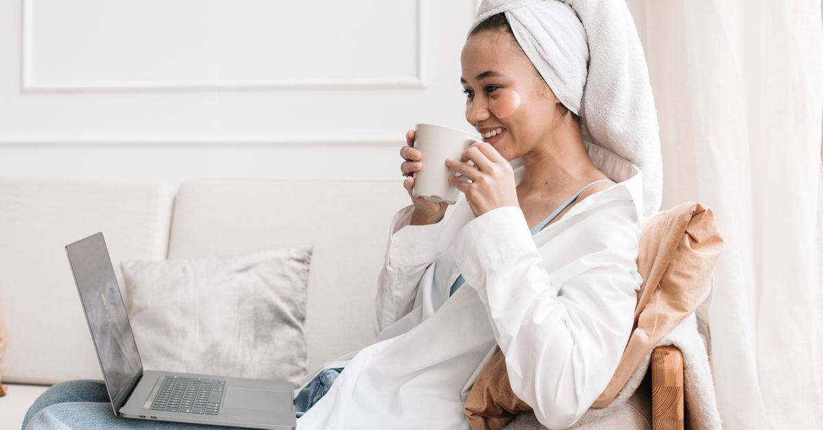 A person opening a laptop with one hand while holding a coffee cup, looking relaxed