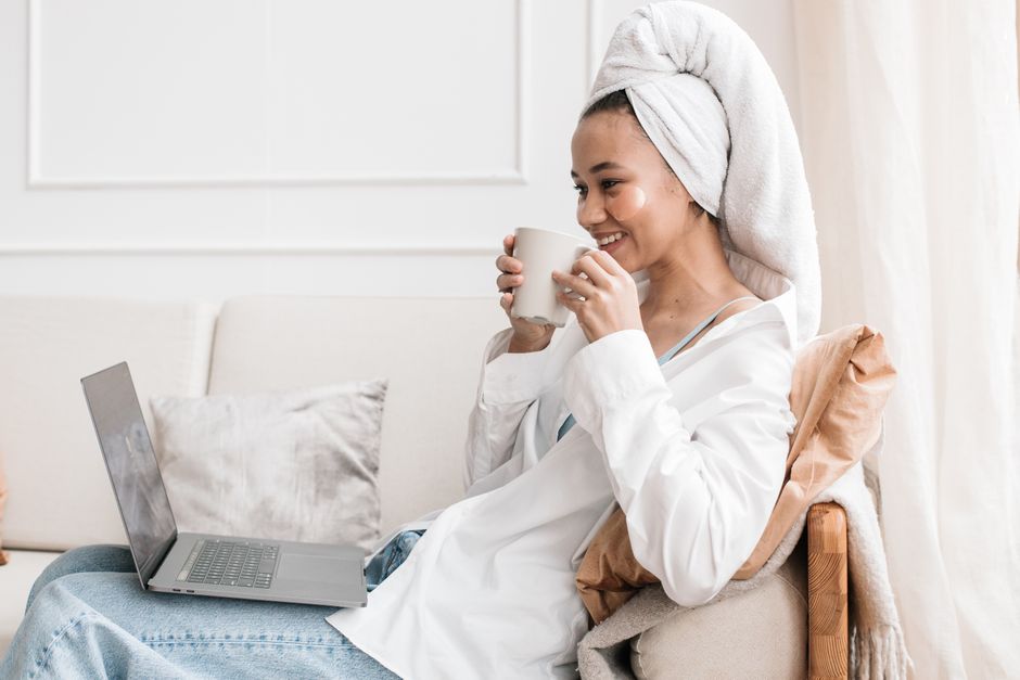 Woman sitting on sofa with coffee, using a laptop, enjoying a serene moment indoors.