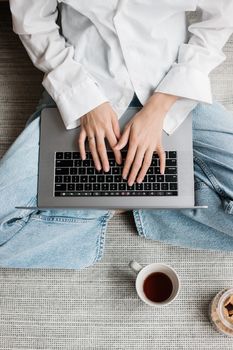 High angle view of hands typing on a laptop, with a cup of tea and snacks, on cozy setting.