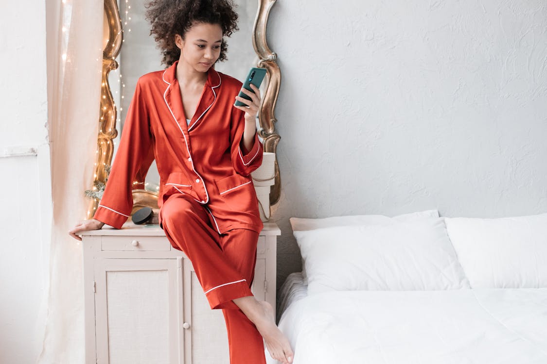 Free Woman in Red Pajamas Using Her Cellphone Near The Bed Stock Photo