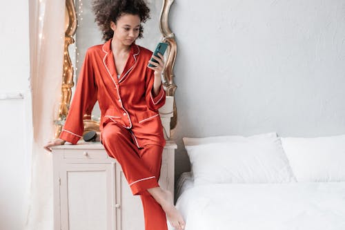 Woman in Red Pajamas Using Her Cellphone Near The Bed