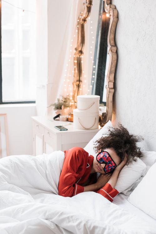 Free Woman relaxing in bed with eye mask, capturing a peaceful morning vibe. Stock Photo