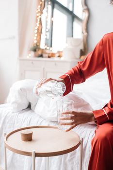 Person in red pajamas pouring water into a glass on a side table, creating a cozy and calm atmosphere.