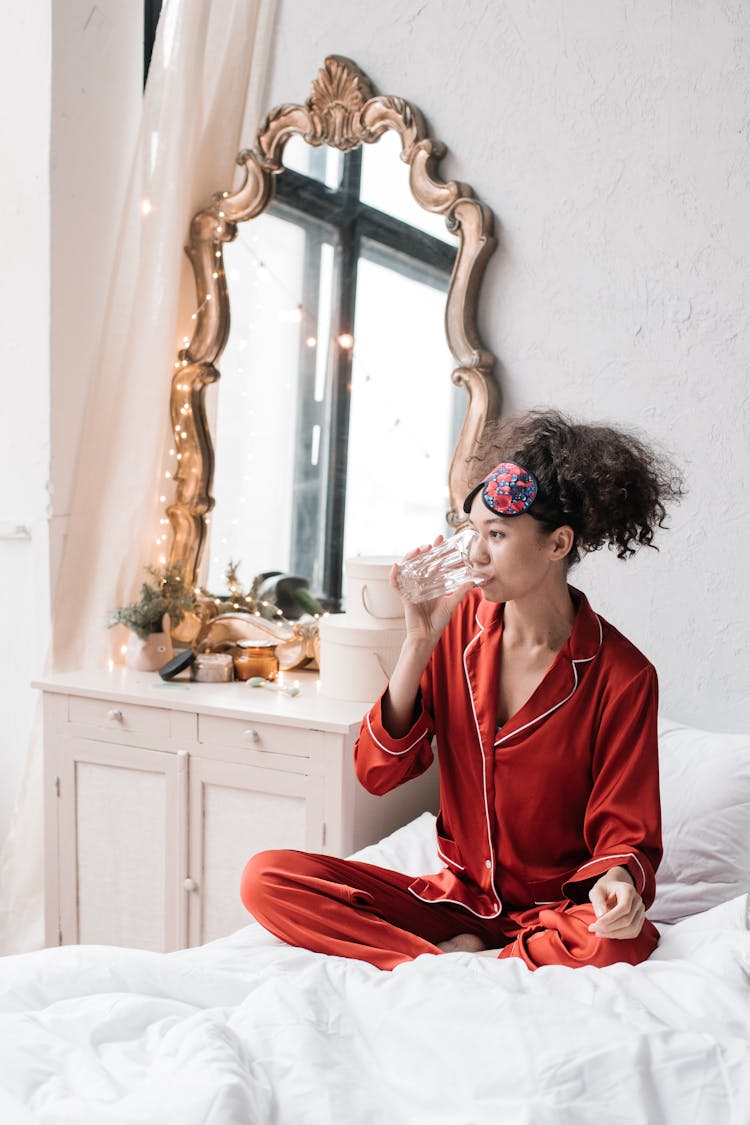 Woman In Red Pajamas Drinking Water In Bed