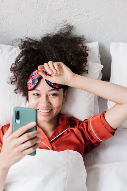 Free Woman in red Pajama Lying on Bed Holding a Cellphone Stock Photo
