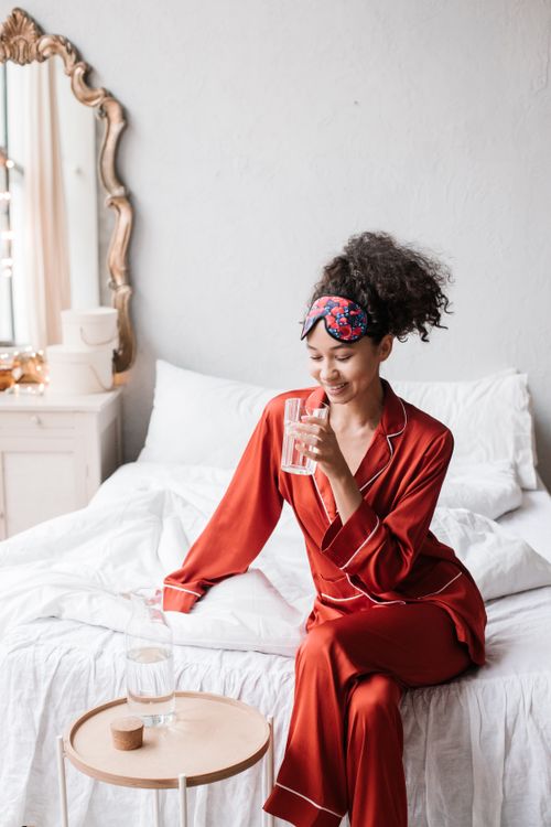 Free Stylish woman enjoying a refreshing drink in cozy red pajamas, bright morning light. Stock Photo