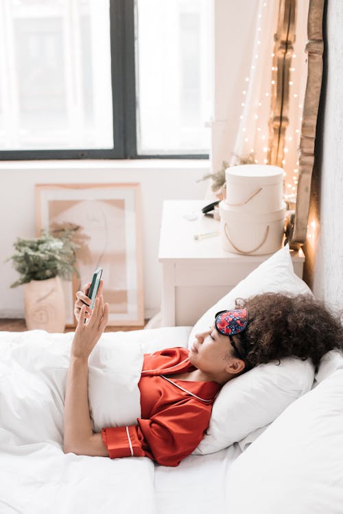 Free A Woman Lying on Bed and using a Smartphone Stock Photo