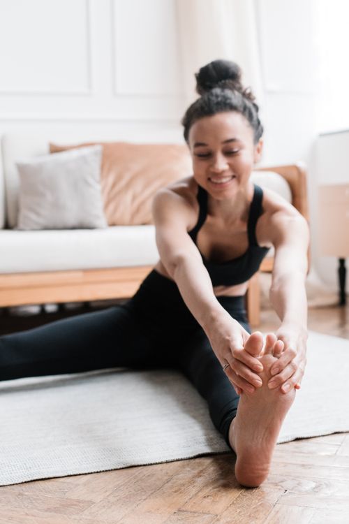 Free Woman performing a yoga stretch on a mat in a cozy living room setting. Stock Photo