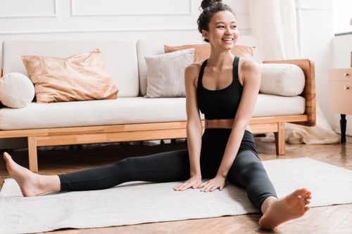 Free Young woman sitting on yoga mat indoors, practicing fitness with a smile. Stock Photo
