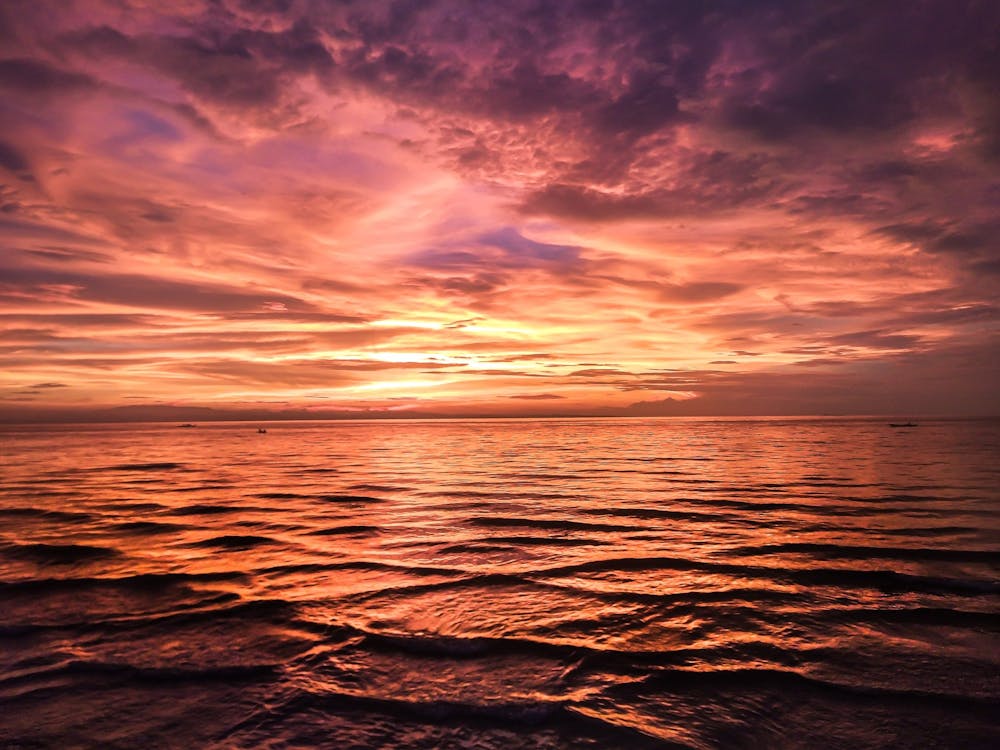 A Body of Water Under a Cloudy Sky During Sunset