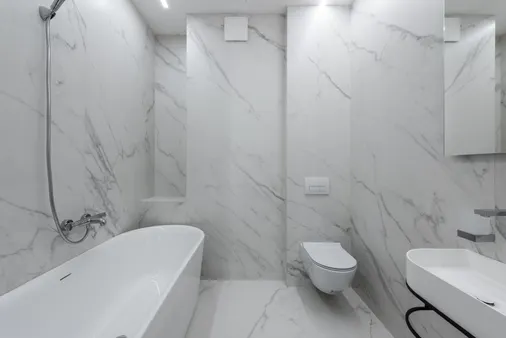 Baño con azulejos de mármol blanco instalados en pared y suelo