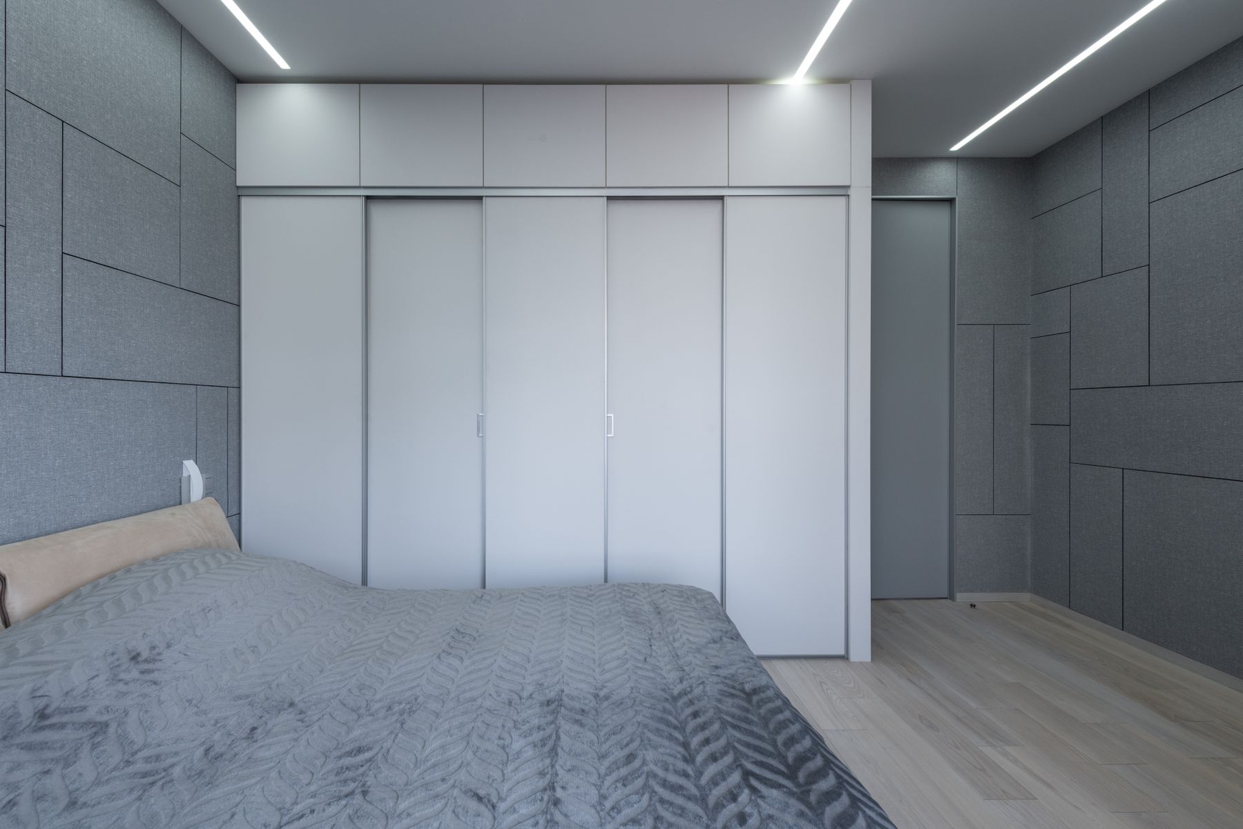 Bedroom with continuous gray wall panels, gray storage fronts and gray bedding beneath linear ceiling lights
