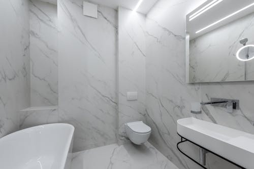 Interior of contemporary bathroom with white bath placed near toilet and washbasin at wall with mirror with reflection at home