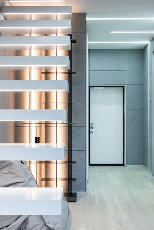 Light living room interior with white stairs near beanbag chair on floor near shelves and door