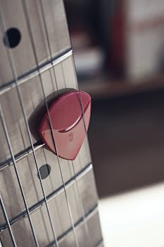 Close-up image of guitar strings with a pink guitar pick placed between them.