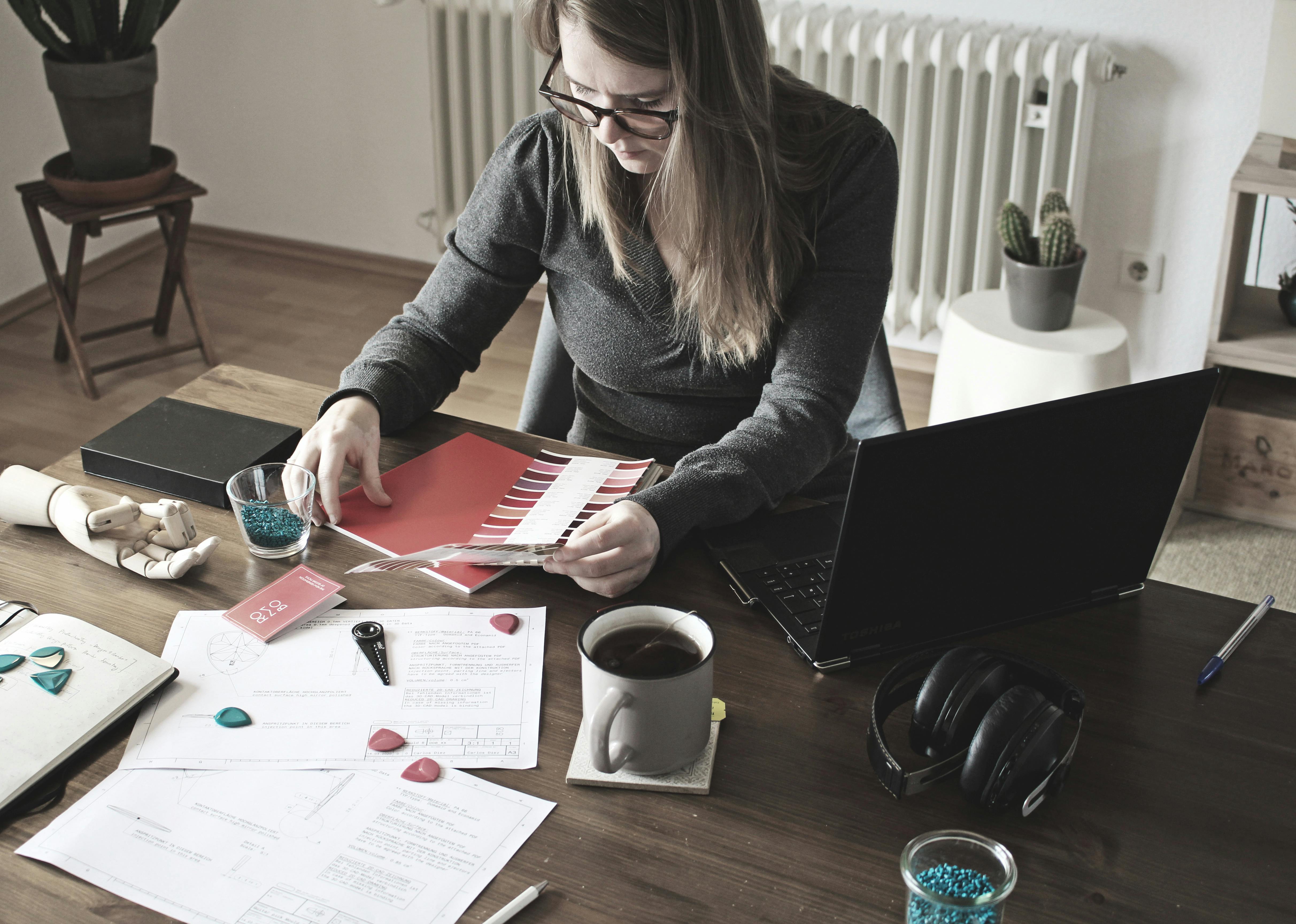 Free Woman working on design project at home office with laptop, papers, and color palette. Stock Photo