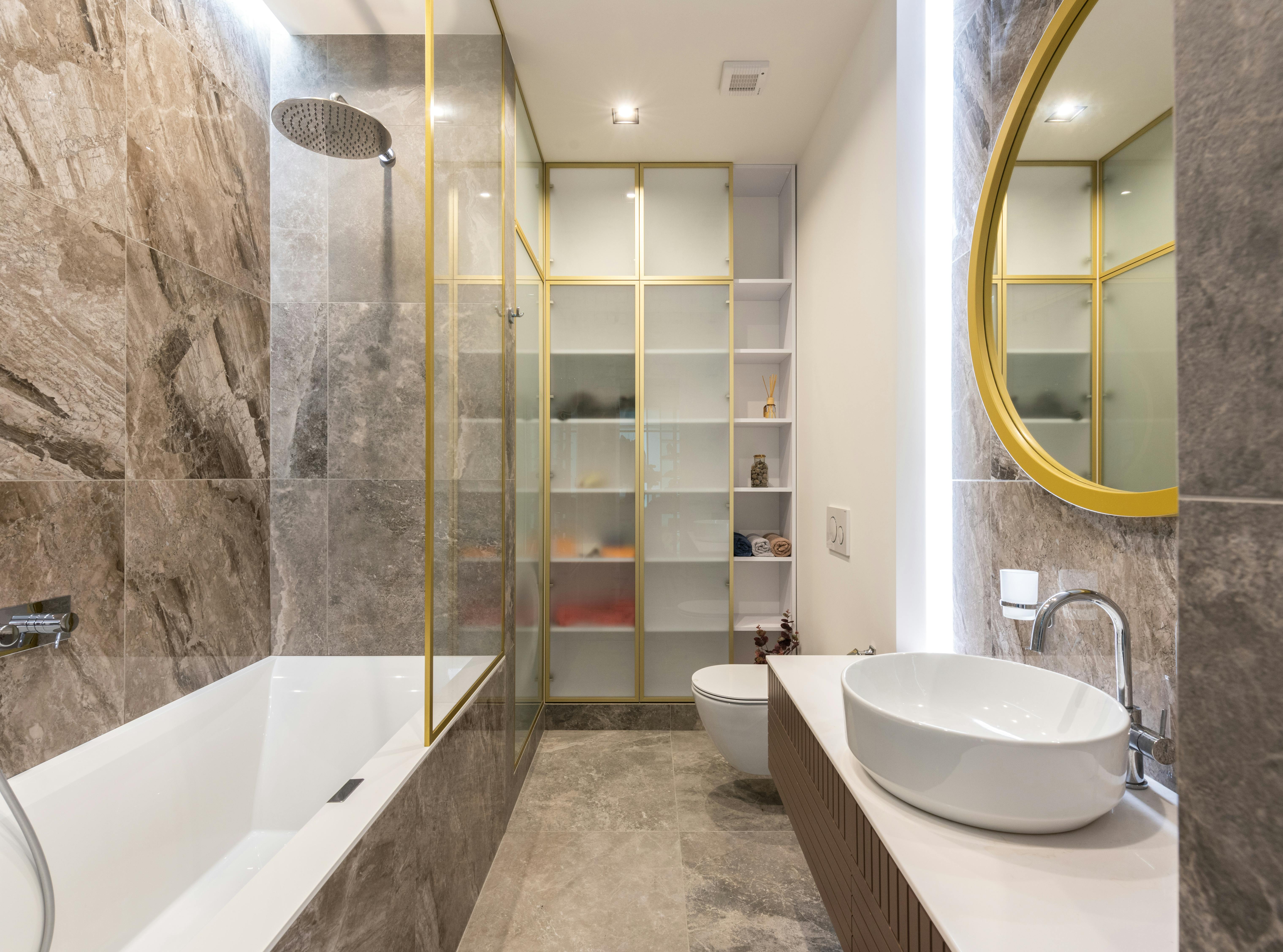 Modern light bathroom interior with white sink and faucet on counter near mirror and toilet near bath