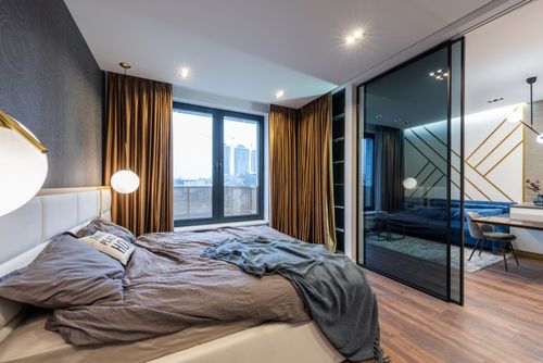 Free Interior of modern bright apartment with bed near pillows and blanket near lamps and glass doors near living room with couch near and window with curtains Stock Photo