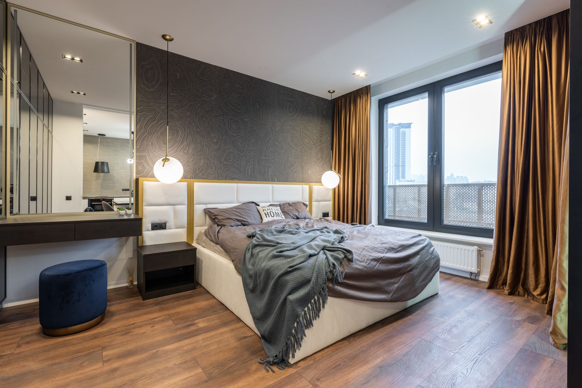 Modern light room interior with soft bed with pillows and blanket near mirror with shelf near pouf and lamps near window with curtains in daylight