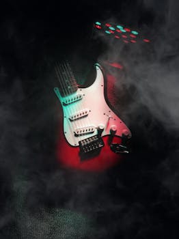 Close-up of an electric guitar in red and green lighting, surrounded by smoke.