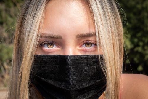 Free A close-up of a woman with blonde hair and green eyes wearing a black face mask outdoors. Stock Photo