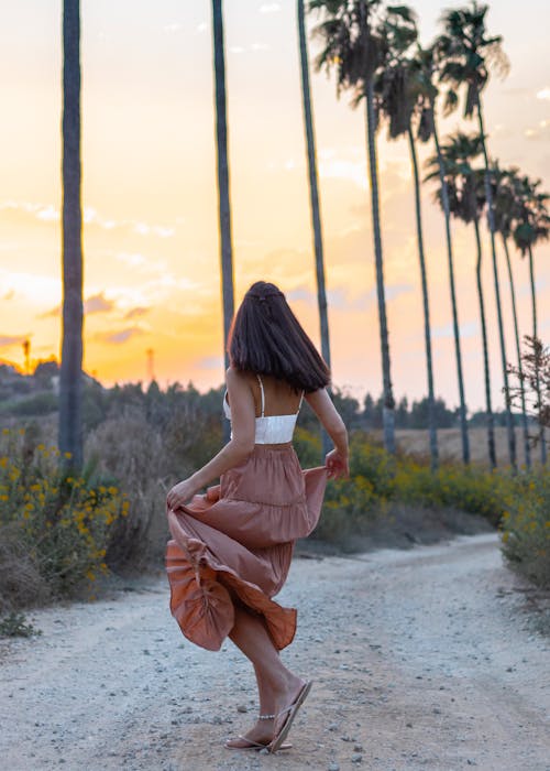 Woman Walking on Dirt Road during Sunset