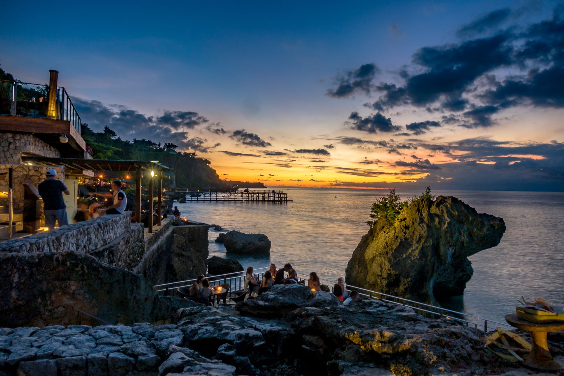 Al fresco seaside dining on a cliff terrace overlooking the ocean at dusk