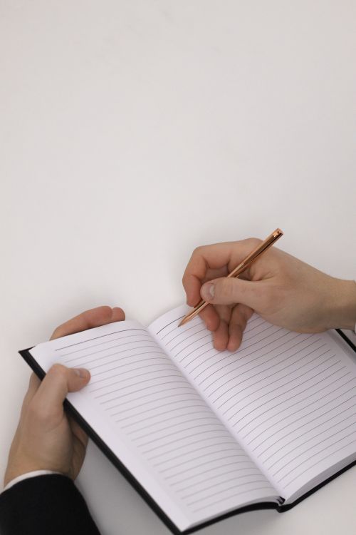 Free Close-up of hands writing in a lined notebook with pen on a white surface. Stock Photo