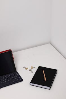 Clean and minimalist workspace featuring a tablet, keyboard, notebook, and paperclips for modern productivity.