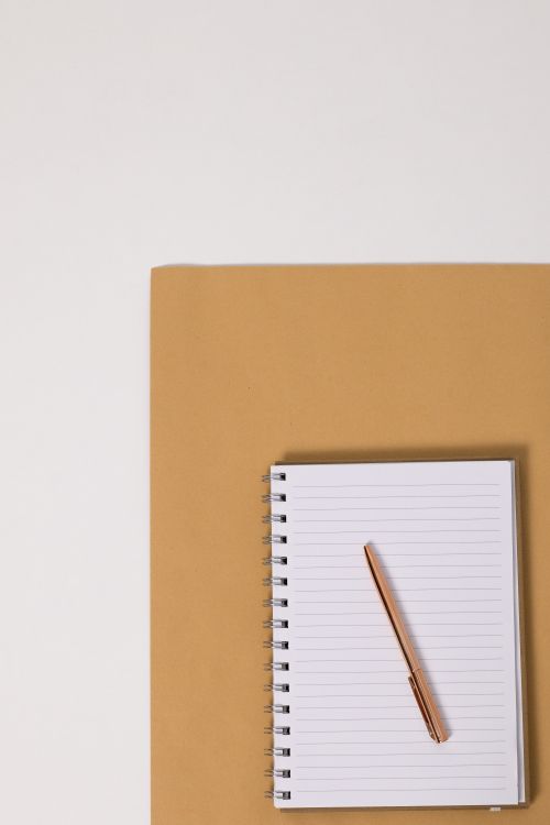 Free Flat lay of spiral notebook and pen on brown surface, perfect for note-taking or journaling imagery. Stock Photo