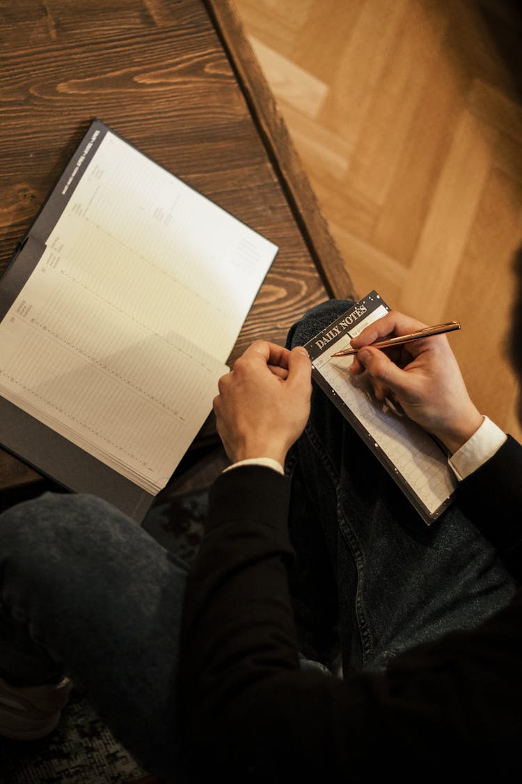 A Person Writing On A Planner