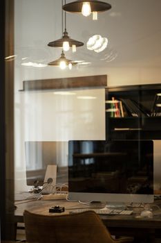 Stylish office setting featuring computers on a desk with elegant lighting fixtures and shelves.