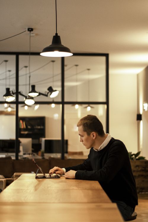 Free A focused businessman working on a laptop in a modern open office environment. Stock Photo