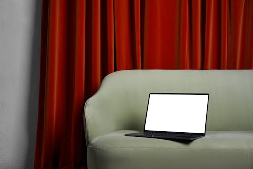 Laptop on couch near red curtains and wall