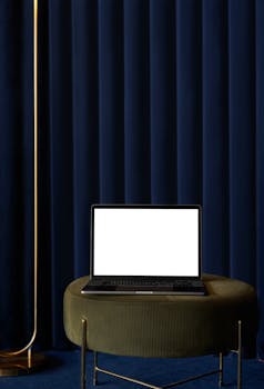 Modern laptop with blank screen on chic table against elegant velvet curtain, perfect for design mockups.