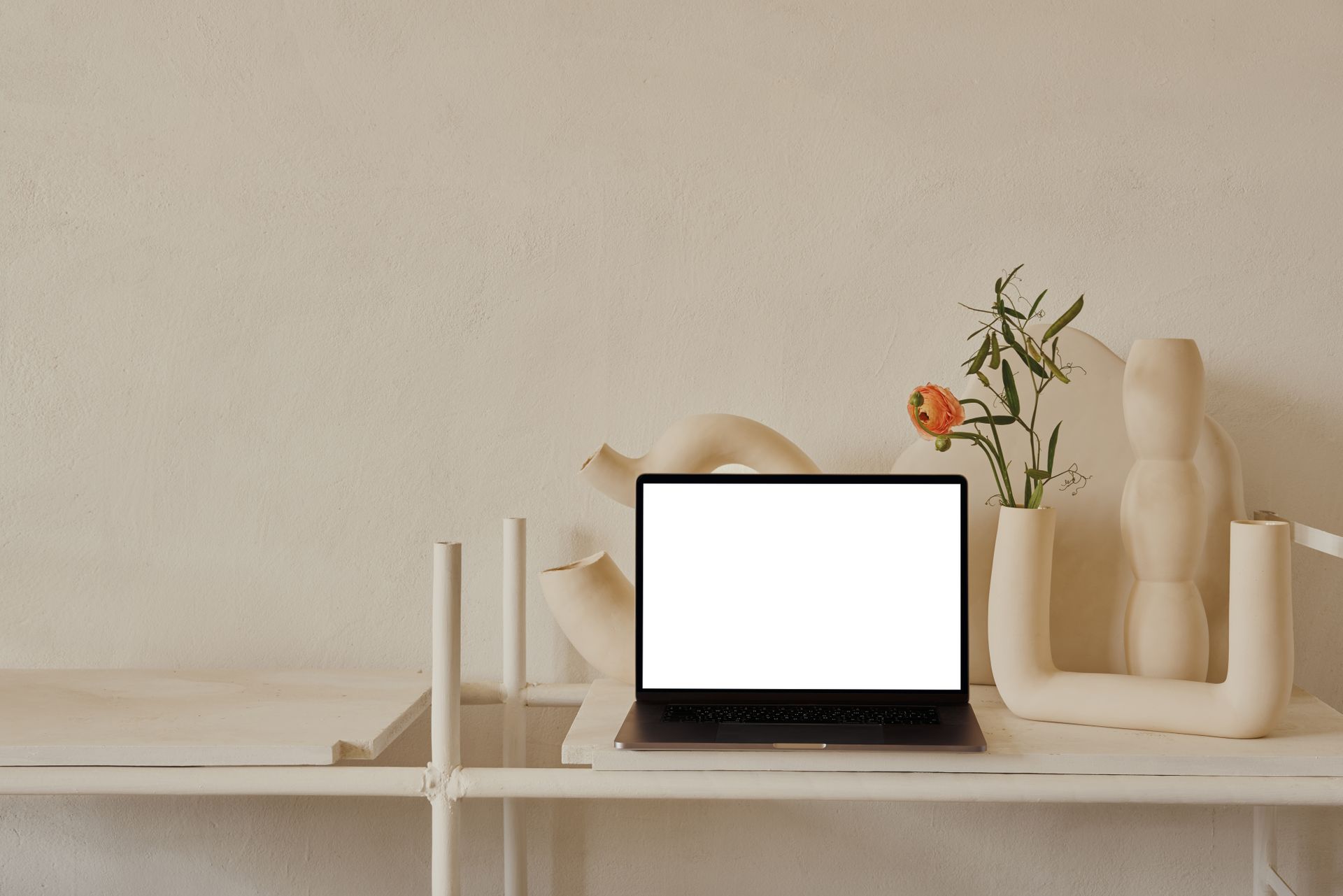 A minimalist workspace featuring a laptop with blank screen and elegant ceramic vases on a neutral background.
