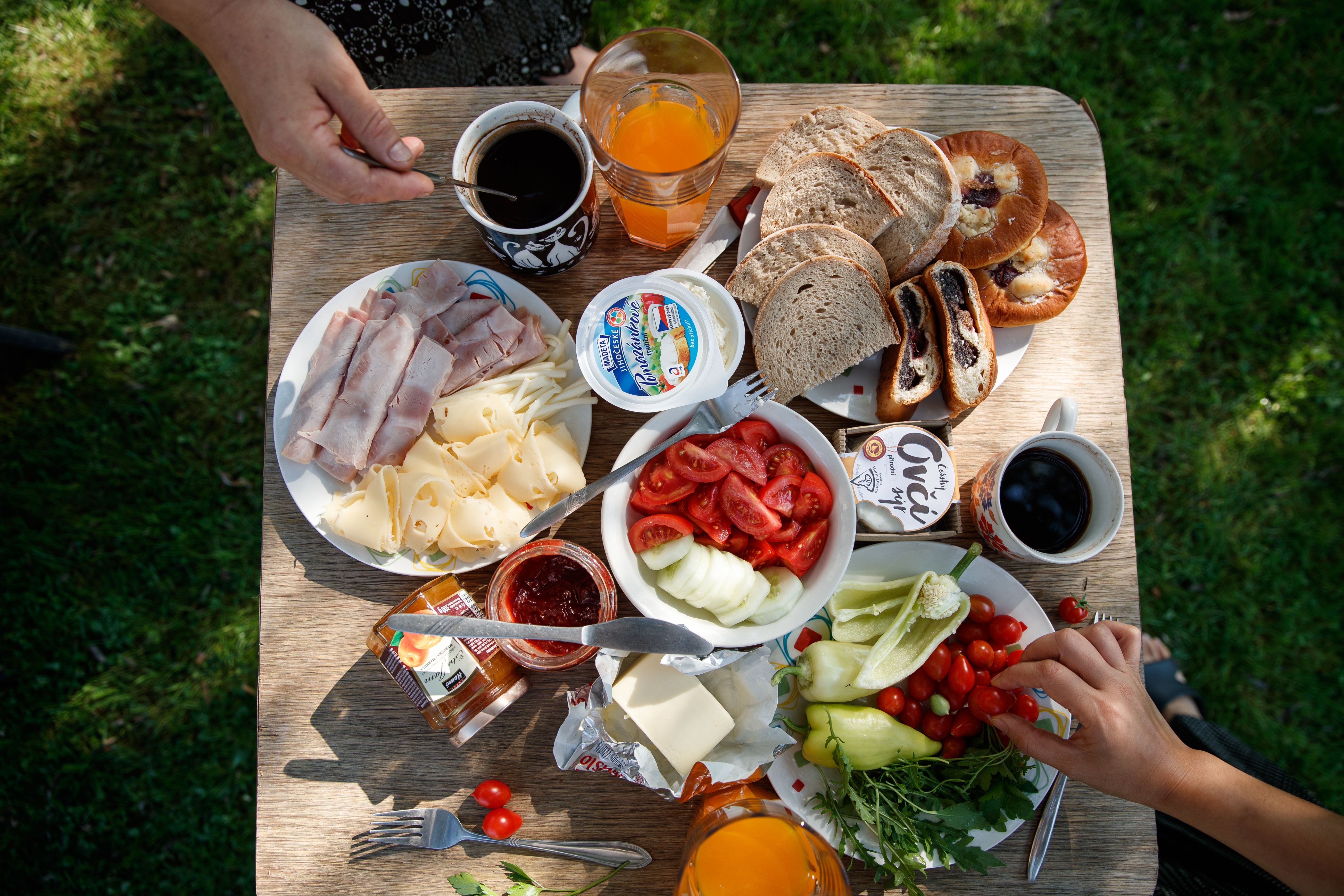 Enjoy a delightful outdoor brunch with bread, cheese, cold cuts, coffee, and fresh vegetables.