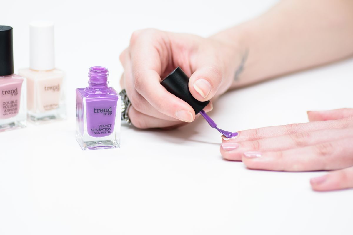 A close-up of a person applying purple nail polish as part of a manicure.