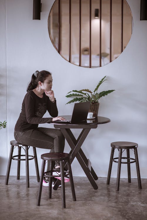 A Woman using a Laptop on a Table while Sitting on a Stool