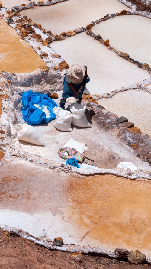 Free A worker collecting salt in Peru's scenic Maras salt ponds, highlighting traditional methods. Stock Photo