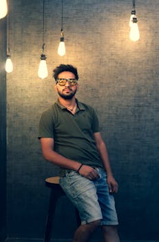 Man in denim shorts and polo shirt poses under warm lights. Indoor setting.