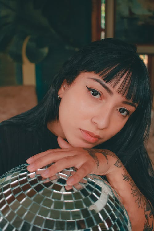 Young woman with tattoo leaning on sparkling disco ball