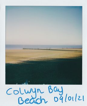 A tranquil view of Colwyn Bay beach captured in a vintage Polaroid style.
