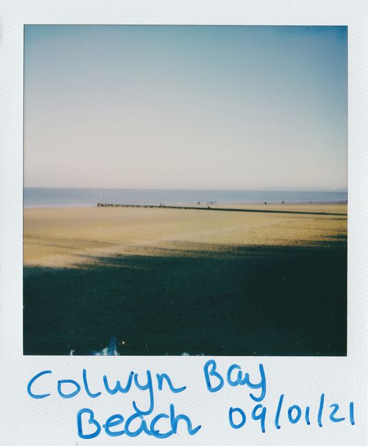 A tranquil view of Colwyn Bay beach captured in a vintage Polaroid style.