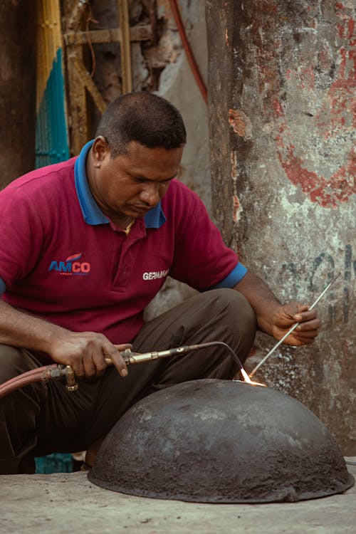 Concentrated ethnic artisan with welding tools fixing cast iron bowl while working on weathered street